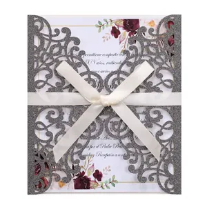 Close-up of laser-cut silver glitter invitation with a white silk ribbon bow