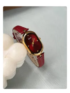 Detail of vintage oval gold watch case with a red sunray dial and leather strap