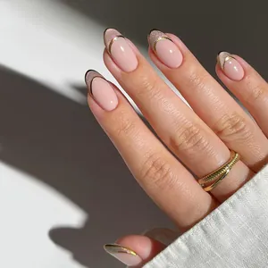 Détail d'ongles en amande rose nude avec pointes French dorées pailletées et liseré doré