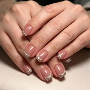 Détail d'ongles en amande rose nude avec des pointes French pailletées argentées et brillantes