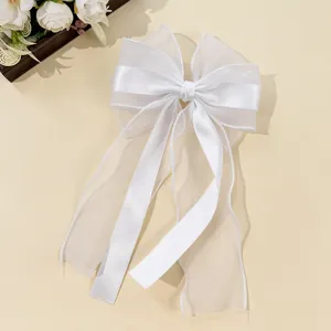 Detail of multi-layer white organza hair bow clip with silky ribbon on cream background