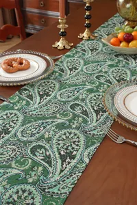 Nahaufnahme eines grünen Paisley-Tischläufers mit Fransen auf rustikalem Holztisch