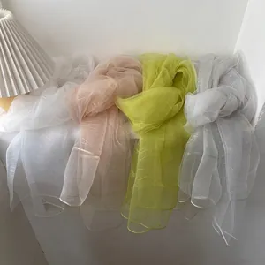 Close-up of lightweight pleated silk scarves in white, pink, green, and grey colors