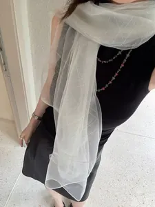 Detail of sheer ivory scarf with fine silver threads worn over a black dress in sunlight
