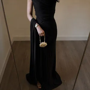 Detail of elegant pleated long black evening dress with a gold shell clutch bag