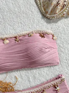 Dettaglio del top bikini rosa arricciato con ciondoli a conchiglia e bordo in pizzo