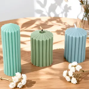 Gros plan de bougies piliers cannelées allumées en vert menthe et olive sur bois