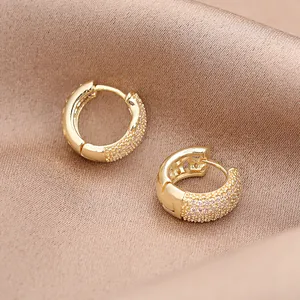 Nahaufnahme von goldenen Huggie-Ohrringen mit Pavé-Kristallen auf Seidenstoff