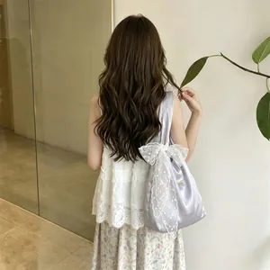 Detail of light purple satin shoulder bag with a large white lace bow and floral embroidery