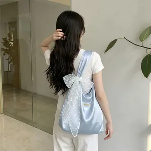 Detail of light blue satin tote bag featuring a large white lace bow on the shoulder strap