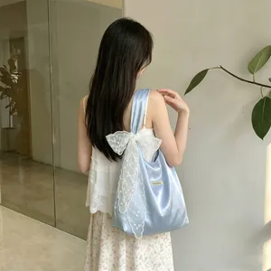 Detail of light blue satin tote bag with large white lace bow and delicate embroidery