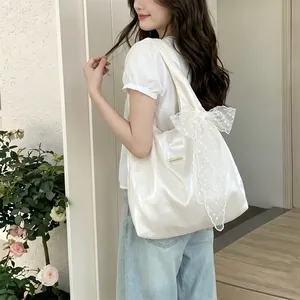 Close-up of cream satin tote bag featuring large lace bow with floral embroidery