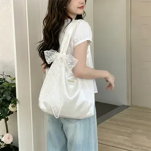 Close-up of a white satin tote bag featuring an oversized lace bow and silk texture