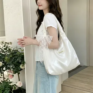 Detail of white glossy shoulder bag with oversized lace bow and silk texture