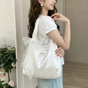 Detail of white satin tote bag with delicate lace embroidery bow and brand label