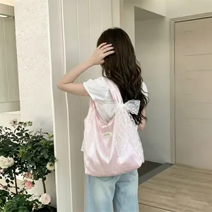 Detail of pink satin tote bag featuring a large white lace bow on the shoulder strap