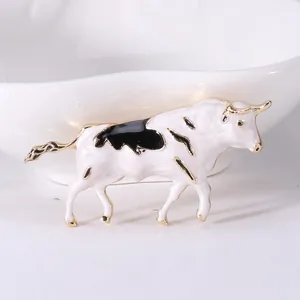 Detailed view of enamel ox brooch with gold trim and white black spotting texture