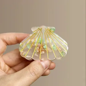 Detailed close-up of shell-shaped acetate hair claw with gold lines and stone inlay