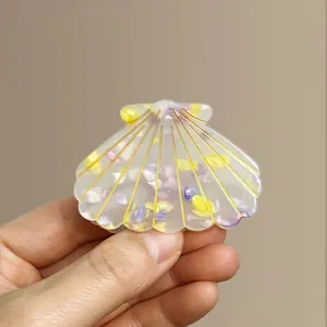 Detail of a shell-shaped acetate hair claw with purple floral patterns and gold lines