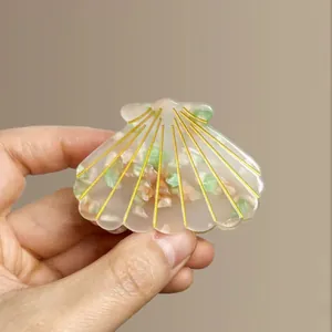 Translucent shell-shaped hair claw clip with colorful confetti and gold ribbed lines