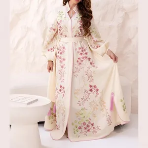 Détail des broderies florales roses et des pompons sur une robe longue blanc crème