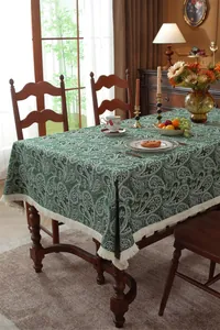 Detail of green paisley tablecloth with white tassel trim on a dark wood table