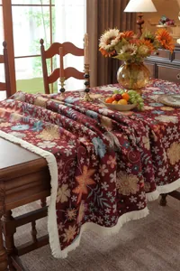 Detail of vintage red floral jacquard tablecloth with fringe on a wooden dining table