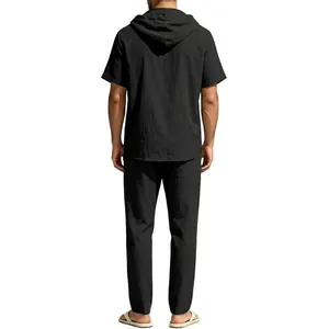 Back view of a man wearing a black hooded short sleeve shirt and matching linen pants