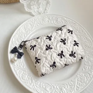 Quilted white cosmetic bag with black bow prints and elegant pearl zipper charm