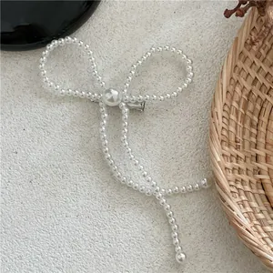 Detail of white faux pearl bow hair clip with ribbons and a silver metal duckbill base