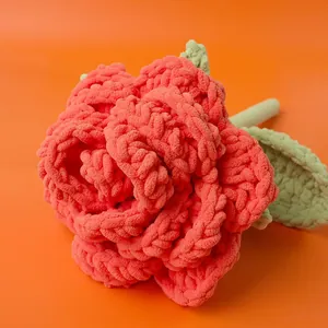 Handmade crochet red-orange rose with green leaves on a warm orange background