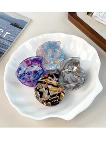Close-up of four acetate hair claws in seashell shapes with elegant marble textures