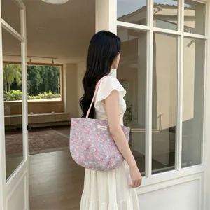 Détail d'un sac cabas en toile à fleurs avec bandoulière rose et étiquette de la marque