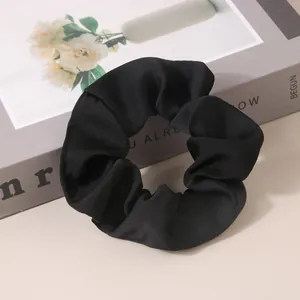 Close-up of a premium black satin scrunchie showing glossy texture and elegant folds