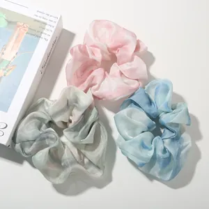Close-up of three satin scrunchies in pink, blue and green with metallic sheen