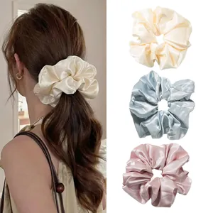 Detailed view of satin silk scrunchies in cream, blue, and pink for women's hair styling