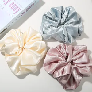 Close-up of premium satin hair scrunchies in light blue, cream, and dusty pink silk texture