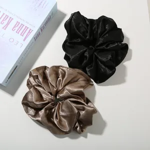 Detail of premium oversized satin scrunchies in black and champagne on white background