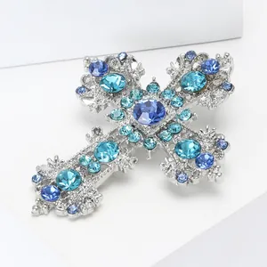 Creative silver alloy cross brooch with blue rhinestones on a white pedestal