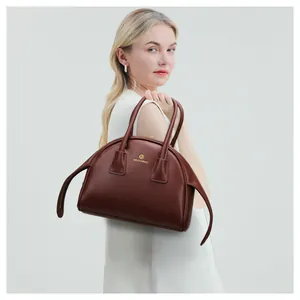 Detail van een diepbruine leren handtas met goud logo gedragen door een model