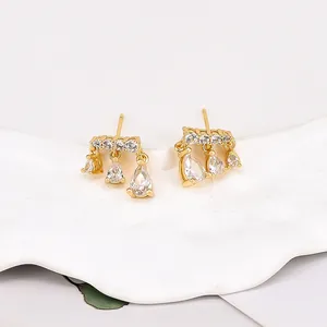 Close-up of gold drop earrings with pear-cut cubic zirconia on a white ceramic tray