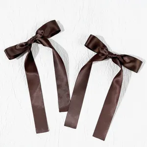 Close-up of a pair of dark brown satin ribbon bow hair clips with long tassels
