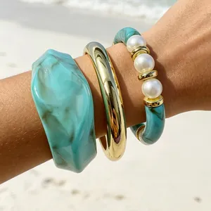 Close-up of bohemian resin acrylic bangle set with white pearls on a beach background
