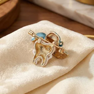 Cartoon tooth brooch with blue hat and white enamel in a polished gold alloy setting