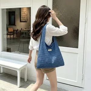 Detail of blue striped corduroy tote bag featuring wide shoulder strap and fabric label