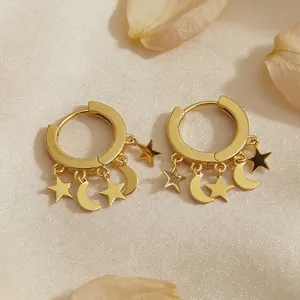 Detail of gold star and moon charms on silver hoop earrings with a silk background