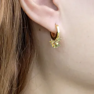 Close-up of gold star and moon hoop earrings worn by a model with long brown hair