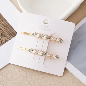 Détail de deux barrettes dorées avec cristaux et nœud papillon sur carte de support