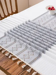 Detail of grey and white hollow crochet table runner with cotton tassels on wood