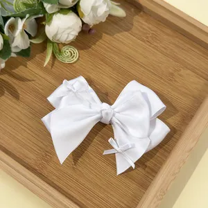 Detail of white satin layered bow hairclip on natural wood tray with floral accents
